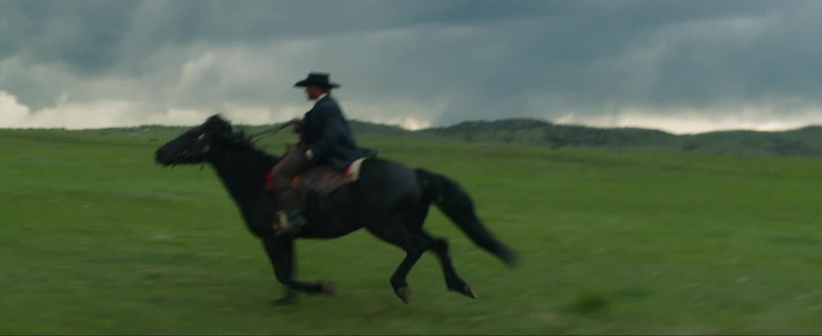 Cowboy rides horse quickly across field under an overcast sky