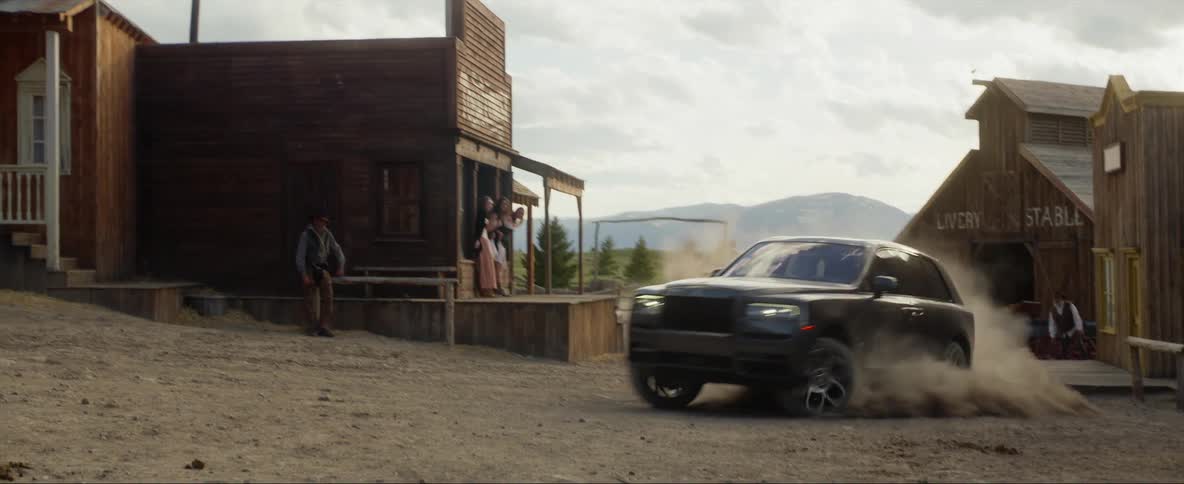 Modern car drives through an old west town kicking up a cloud of dust