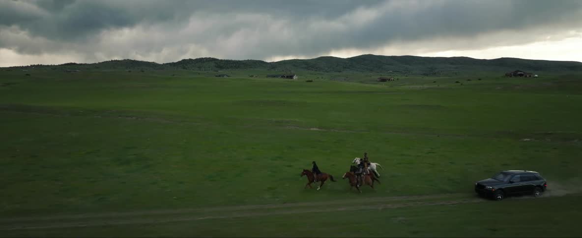 A vehicle speeds past a group of people riding horses through an open field