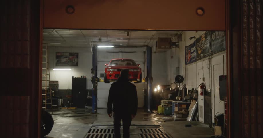 Man walks into mechanics garage as door opens to show car on lift
