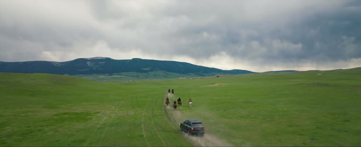 Modern vehicle chasing after cowboys riding on the green plains towards the horizon