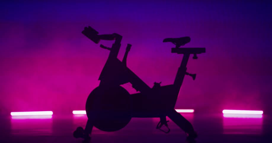 Silhouette of an exercise bike on a stage with lights and pink and purple smoke in the background