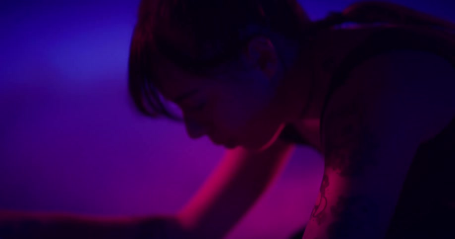 Sihlouette of a young woman pedaling on a static bicycle under colorful lights