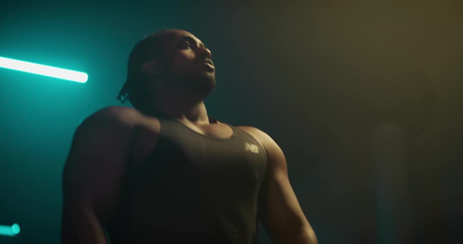 Young strong muscular man stand idle on a dimly lit gym looking at the camera