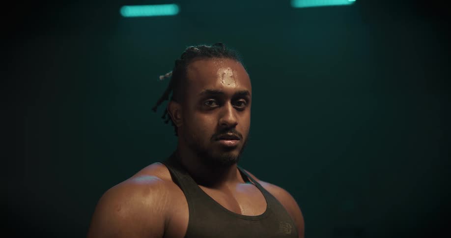 Muscular and sweaty man breathes heavily and looks at camera in the gym