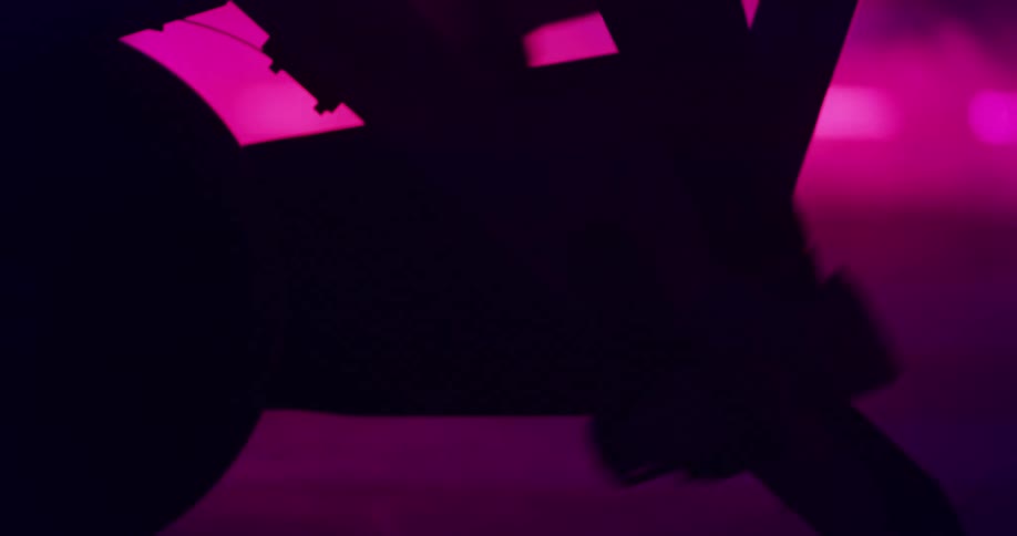Woman on exercise bike is silhouetted against the led lights in the gym