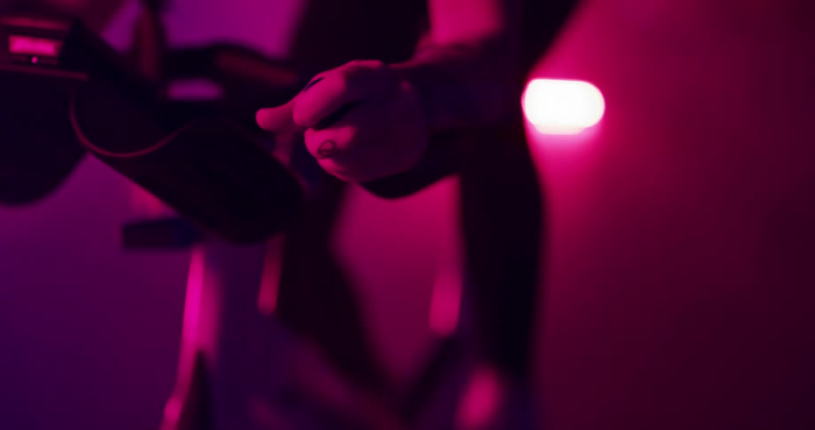Young tattooed woman pedals intensely on a static bicycle una room full of smoke and colorful lights