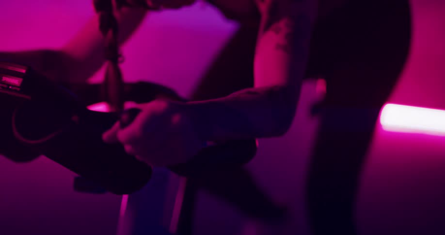 Woman pedals an exercise bike in a space illuminated by pink and purple lights
