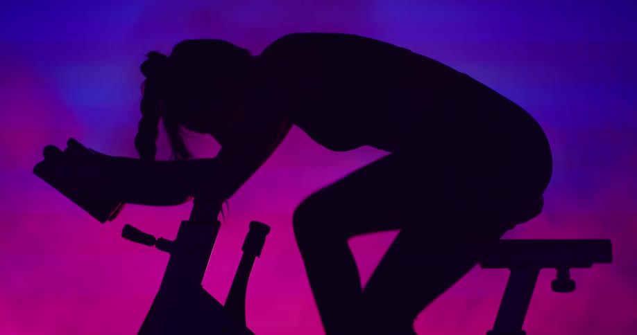 A woman in silhouette rides an exercise bike against a gradient pink and purple background