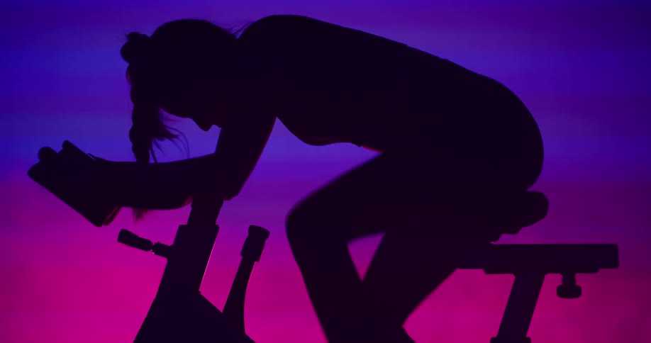 A woman on a spin bike speeds up her legs and puts her head down as she exercises