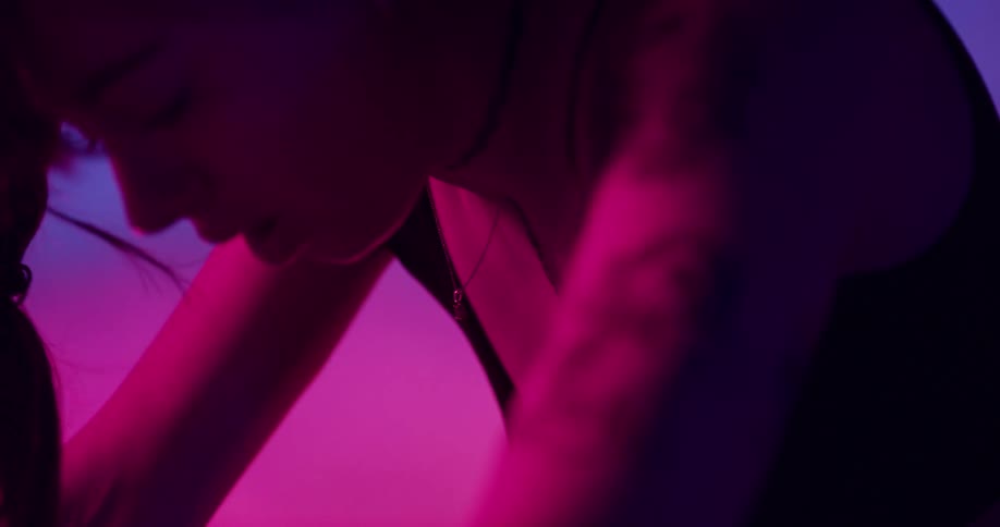 Woman sitting on stationary bikeunder colored lighting catches her breath as smoke spreads in the background