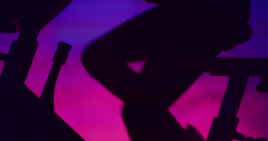 Determined woman on exercise bike is silhouetted against the led lights in the gym