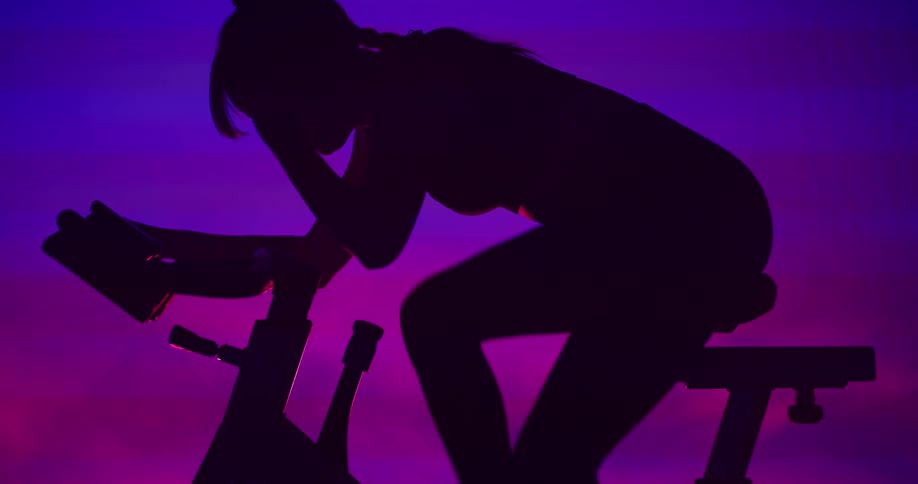 A silhouetted woman working out on a stationary bike