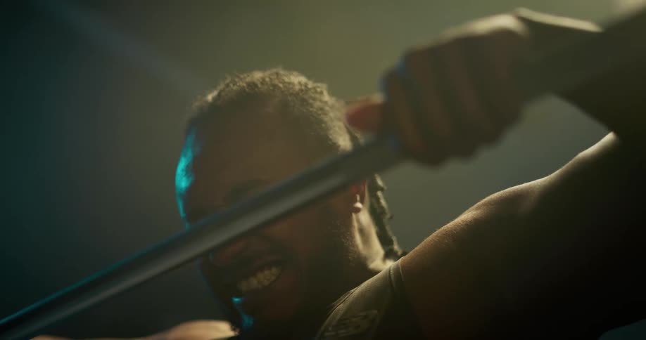 Light shines on a man as he is working out weight lifting with a barbell