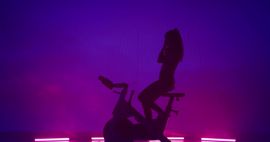 Silhouette of a woman training on a static bicycle stopping to rest and drink water