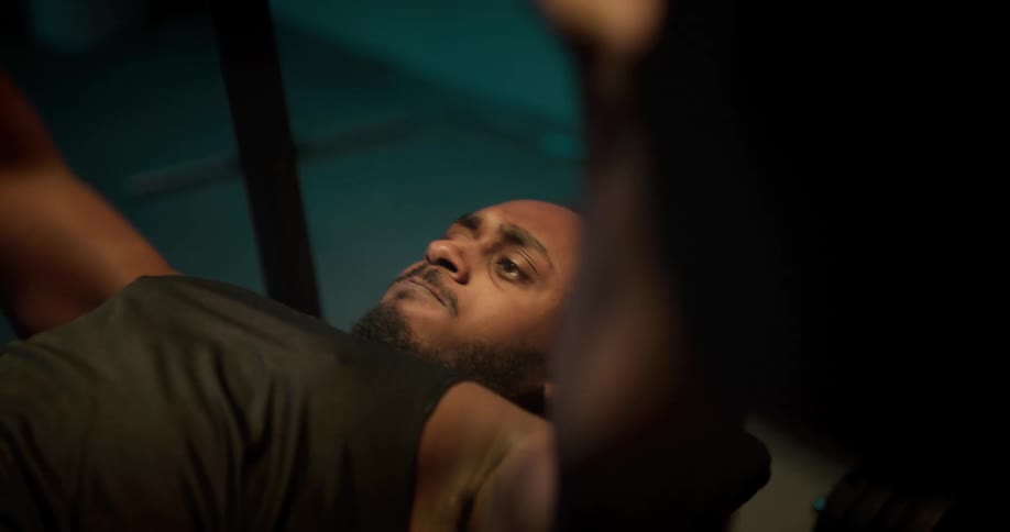 A man lifts weights on a weight bench in a dimly lit room