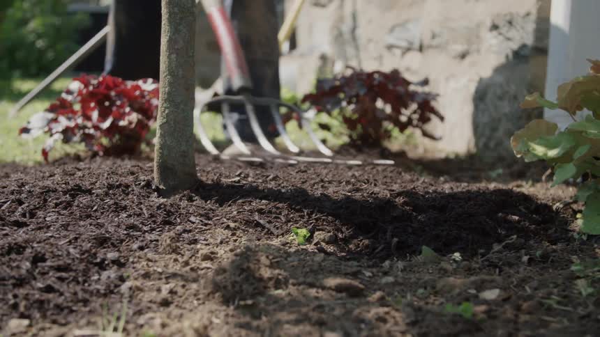 A person is gardening moving dirt around with a pitchfork
