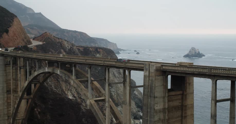 Car driving over a bridge in the mountains next to the ocean at evening