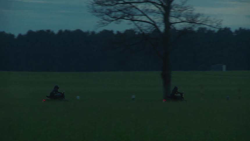 Two motorcyclists drive quickly along a remote road near an expansive forest