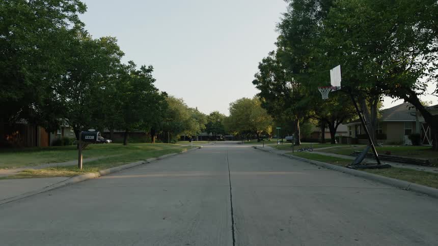A quiet, rural neighborhood street lined with trees and houses