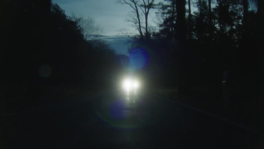 Car illuminating the road drives on highway in the woods at dusk
