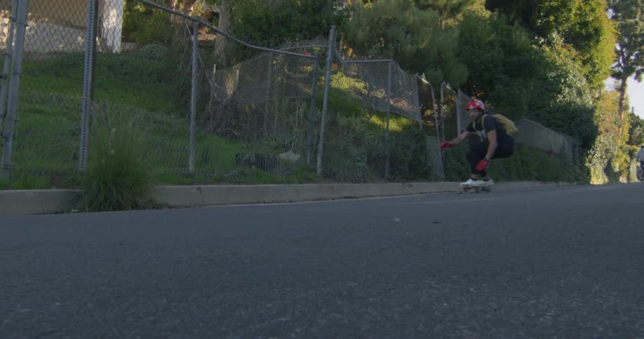 Man with red helmet black t shirt pants and red gloves rides on skateboard down the road