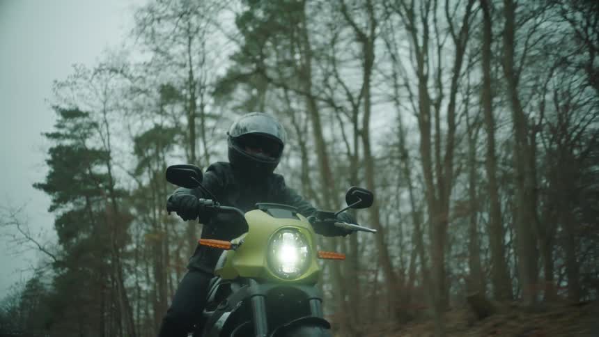 Person rides a motorcycle on a rural road surrounded by forests