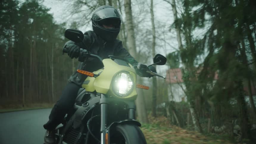Biker wearing black helmet leather jacket and pants rides motorcycle on country road