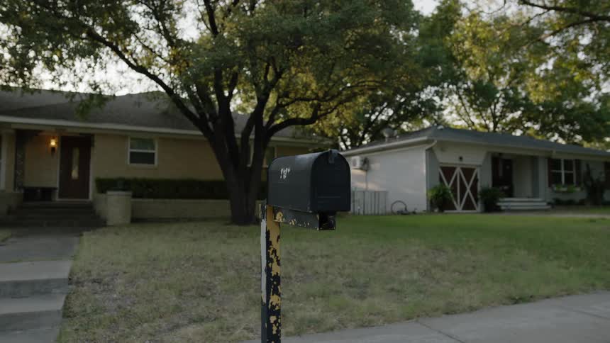 Black mailbox on a peeling post in front of house in a rural neighborhood at sunset