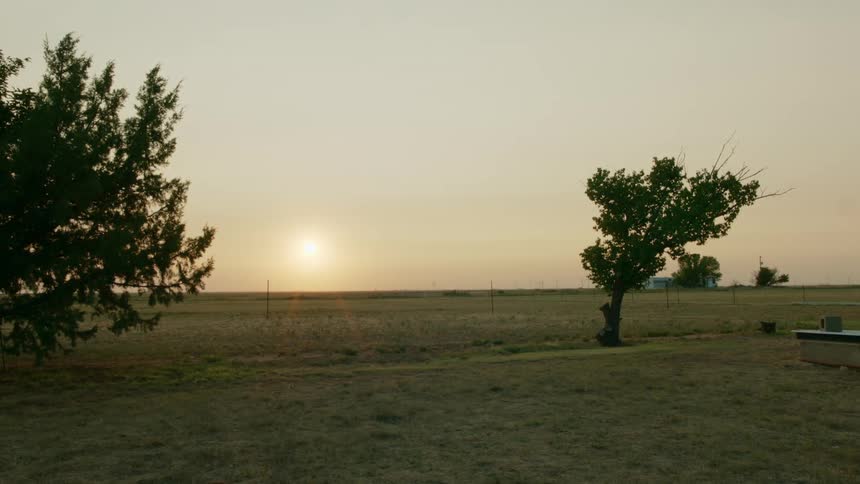 Sun setting on the horizon over a calm grassland field in the rural countryside of Texas