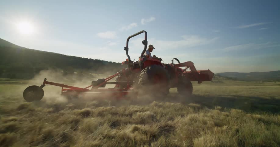 Man drives machinery across field stirring up dust on a sunny day