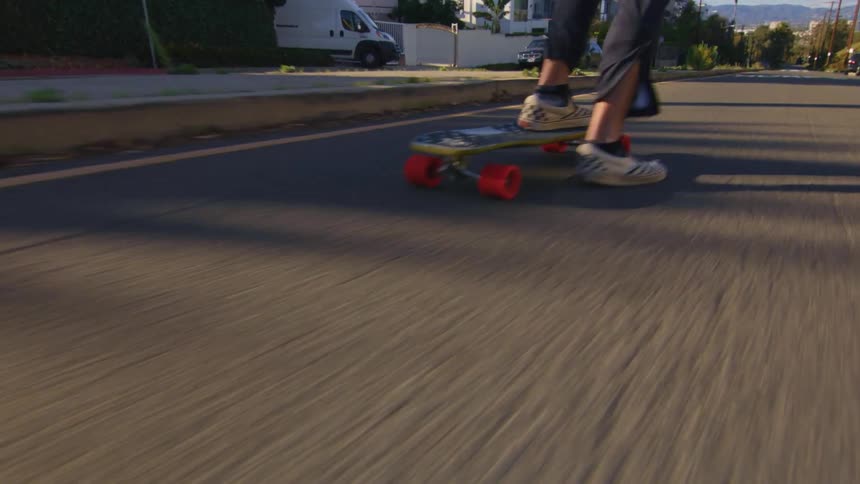 A person rides a skateboard down the middle of a neighborhood street