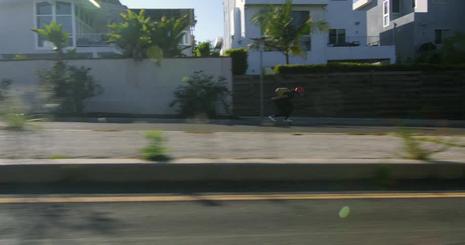 Man in red helmet and black backpack skateboards down the street