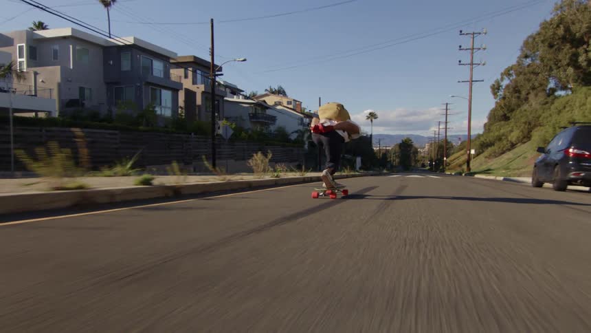 Skateboarder rides along street toward horizon while passing apartment buildings
