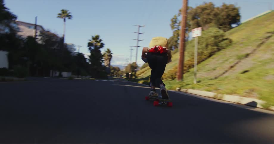 A teenage boy wearing a backpack is riding his skateboard on a neighborhood street