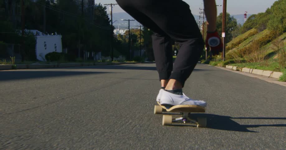 A skateboarder crosses the street while riding down a sloped road