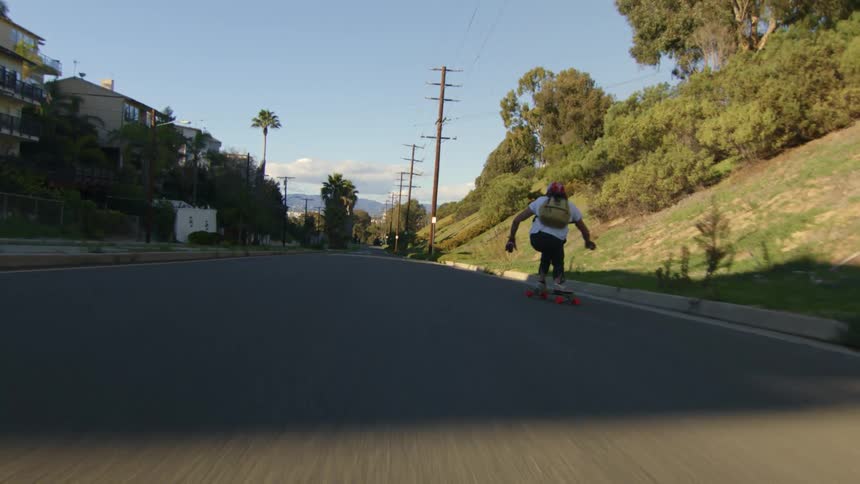Man with red helmet white shirt black pants and red gloves rides on skateboard down the street