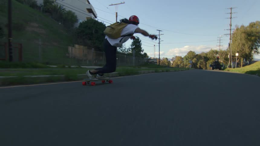 A teenager wearing a backpack is riding his skateboard on a neighborhood street and swaying back and forth as they move on the road