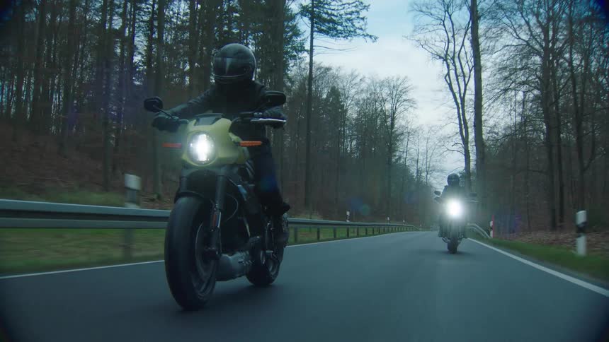 Two cyclists are riding motorcycles on a road through the woods