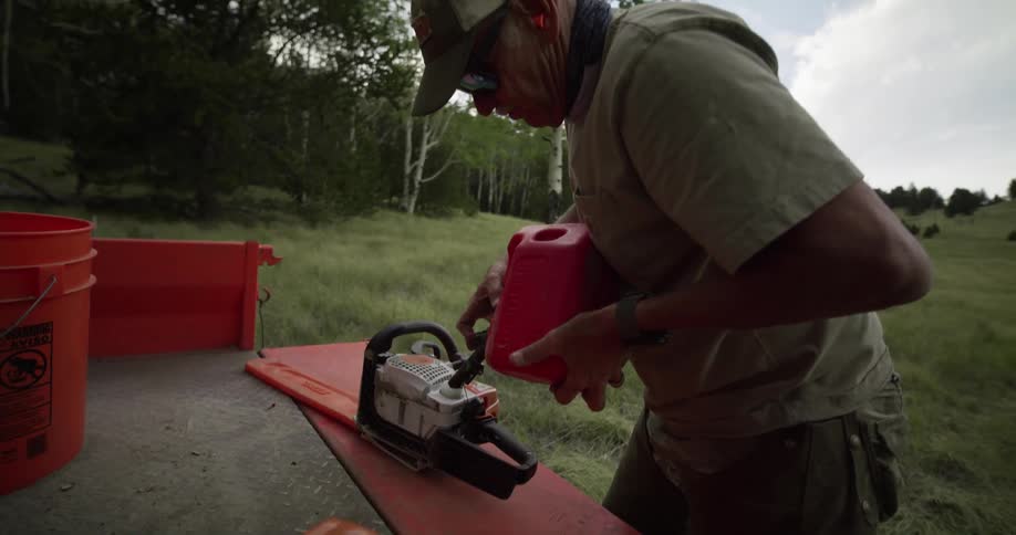 Elderly man uses a gas canister to fill up a chainsaw on the back of a pickup truck