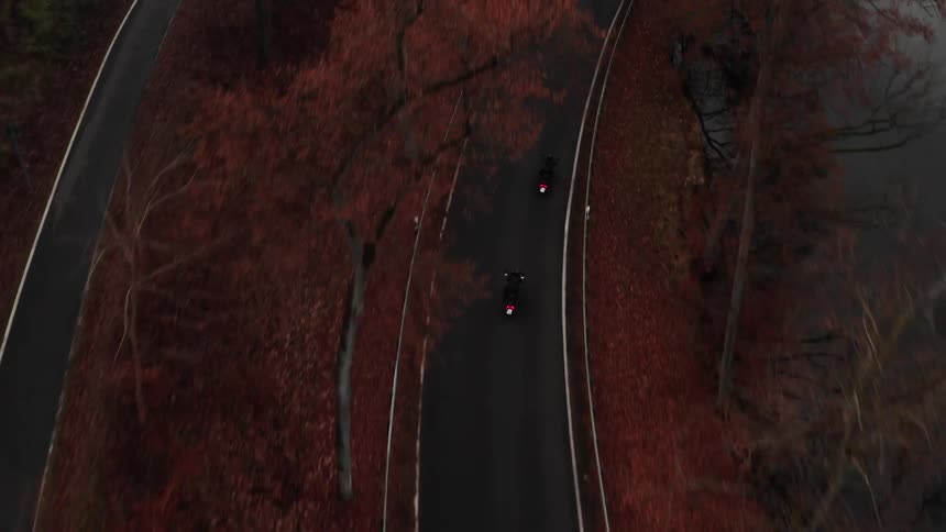 Aerial view of a couple of motorcycles driving on a road near a lake at evening