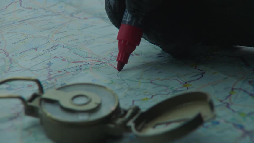 Gloved hand drawing a route line on map with a red marker