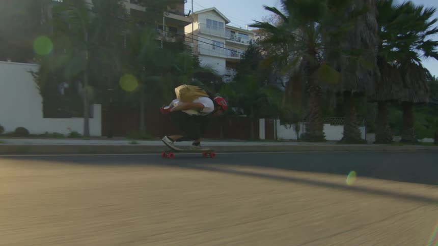 Man in red helmet white t shirt black pants and red gloves rides on skateboard down the street