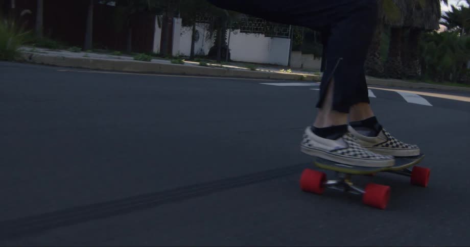 A teenager is bending down as he rides his skateboard on a neighborhood street