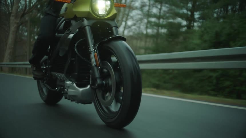 Biker rides motorcycle on highway next to forest