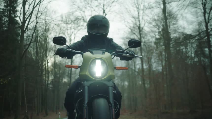 A motorcyclist rides a motorcycle through a woodland on an autumn day