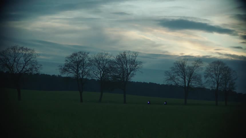 Motorcycles are driving through a rural area at dusk