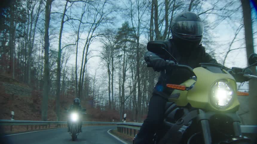 A pair of motorcyclists travel along a road through the countryside on an autumn day