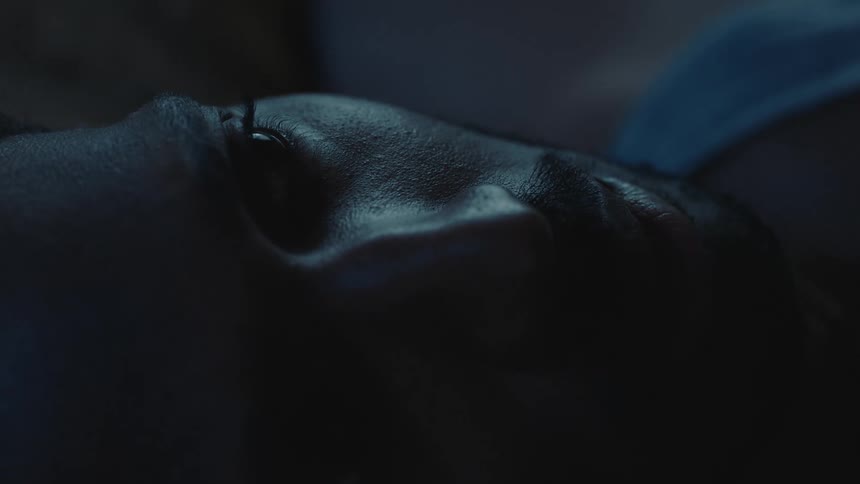 Man lying in dim room with his eyes shut opens his eyes