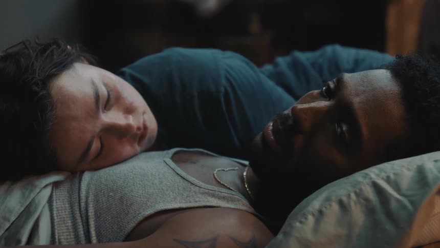 Woman lies with her head on chest of staring man as they occupy bed